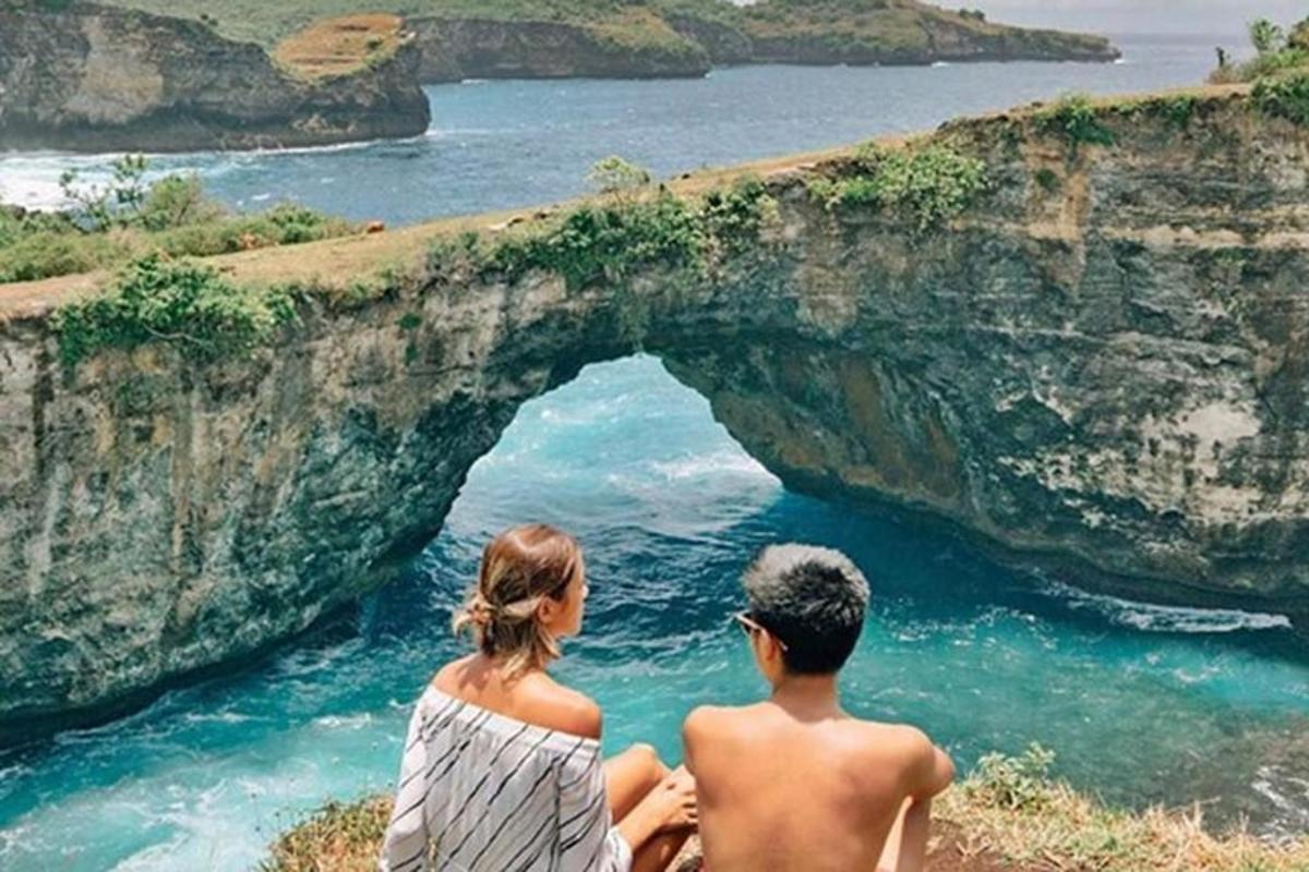 seorang lelaki dan wanita duduk di atas tebing melihat lautan