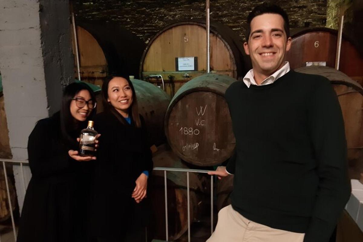 Un hombre y dos mujeres de pie frente a barriles de vino.