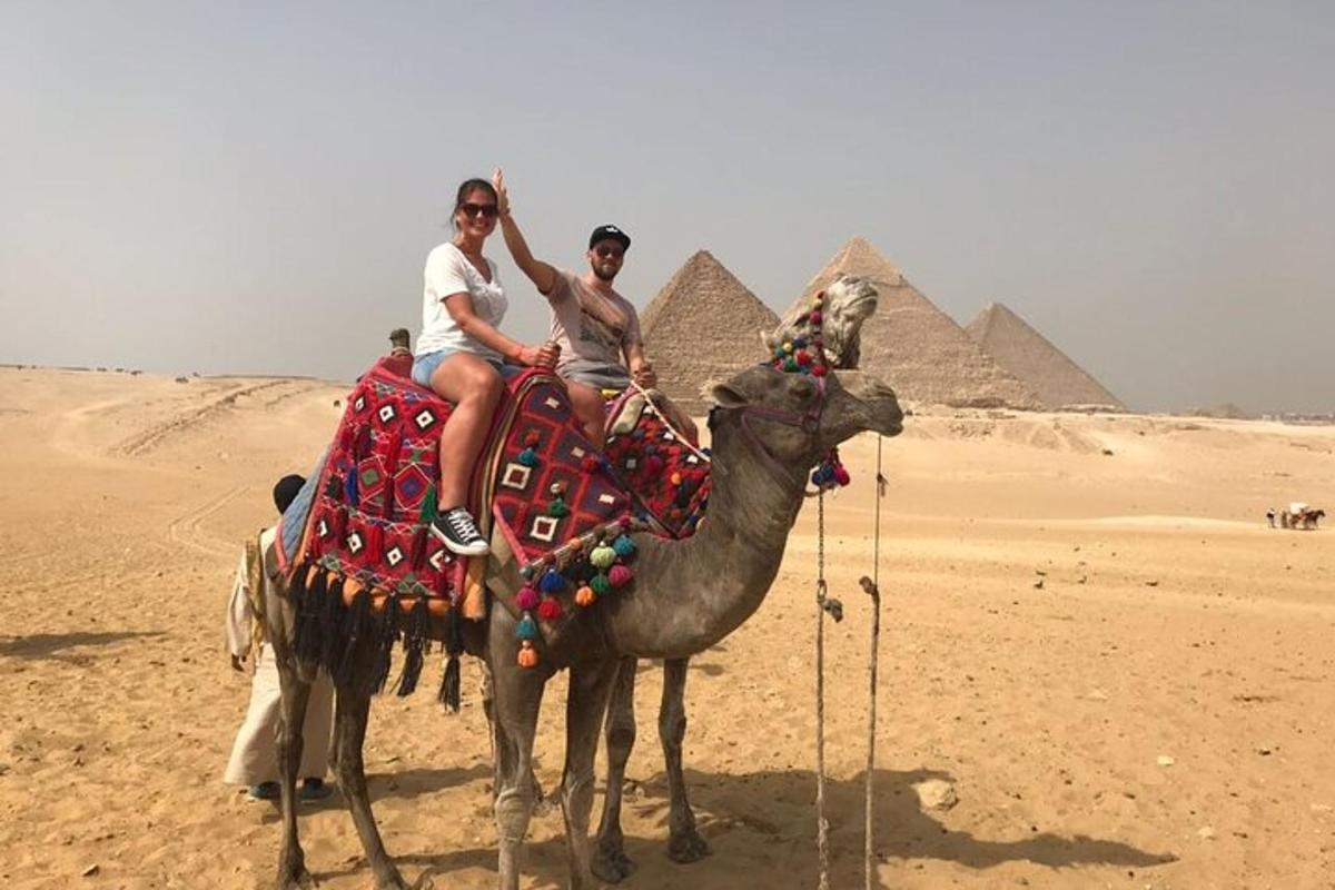 dvaja ľudia jazdiaci na ťave pred pyramídami