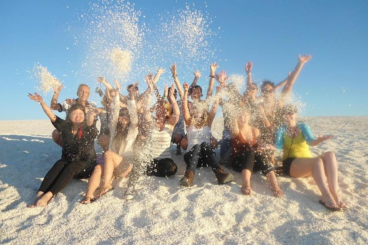 een groep mensen die in het zand op het strand zitten