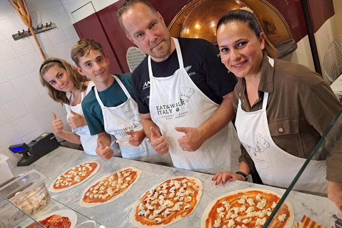 um grupo de pessoas em pé em uma cozinha com pizzas