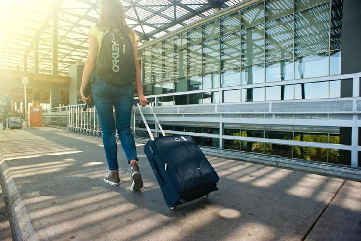 μια γυναίκα περπατάει στο πεζοδρόμιο τραβώντας μια βαλίτσα