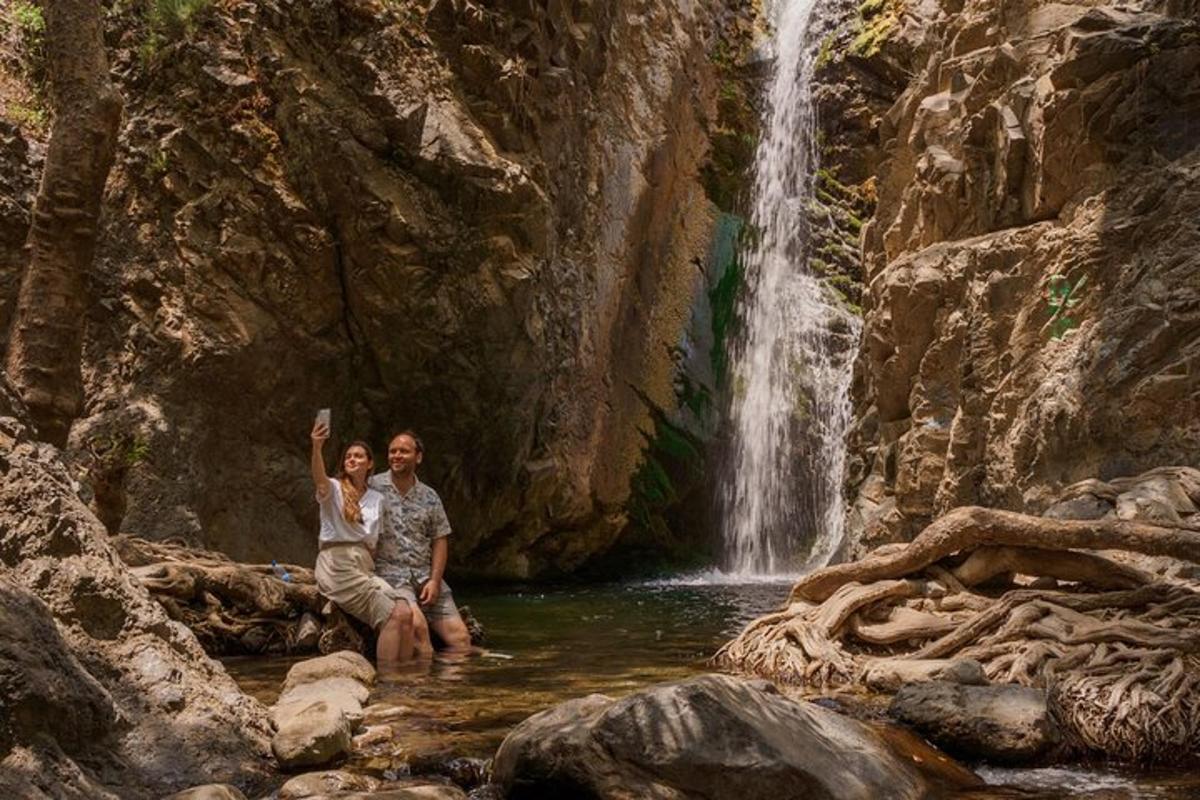 a man and woman sitting in a stream in front of a waterfall