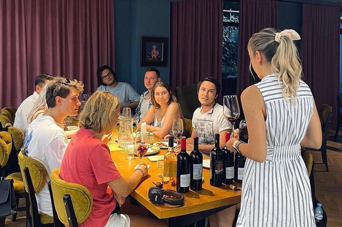 cilvēku grupa, kas sēž ap galdu ar vīna pudelēm