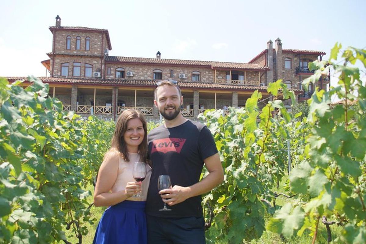 un uomo e una donna in piedi in un vigneto con in mano dei bicchieri di vino