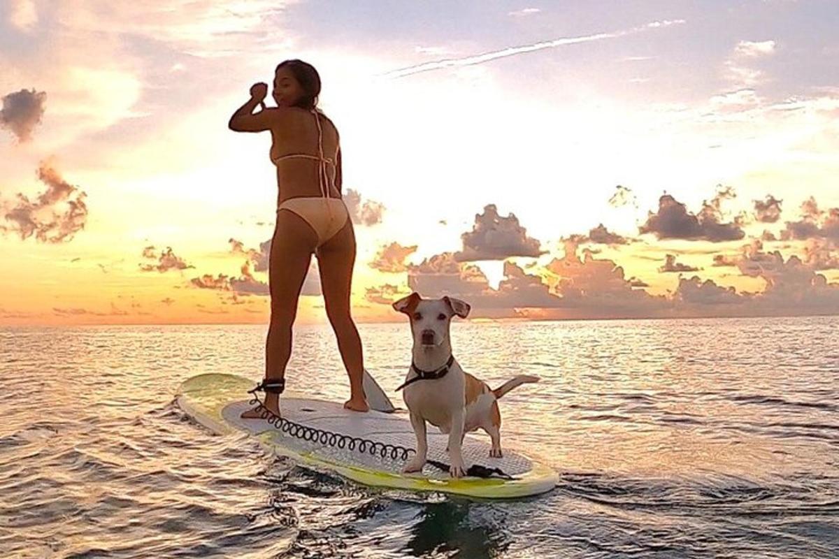 Una mujer y un perro en una tabla de surf en el agua