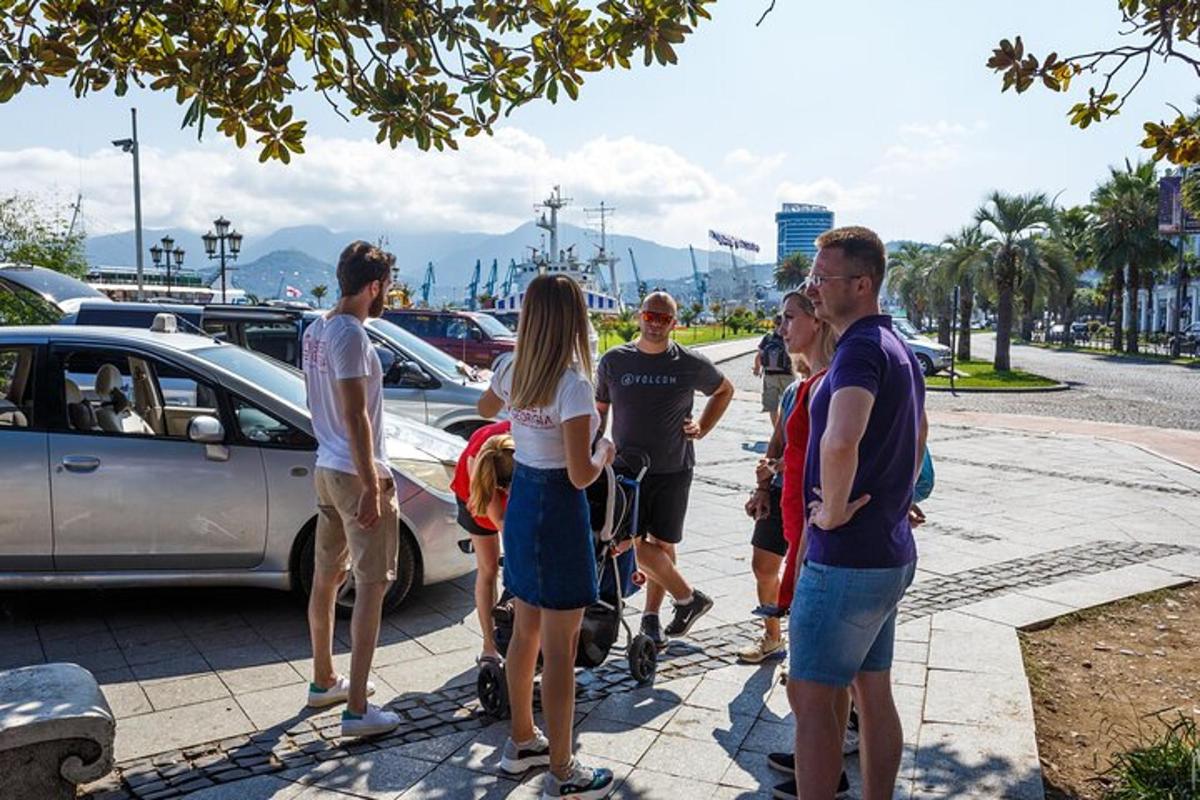 a group of people standing on a sidewalk near a parking lot