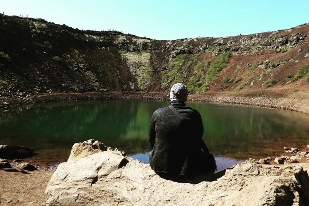 maður situr á steini nálægt vatni