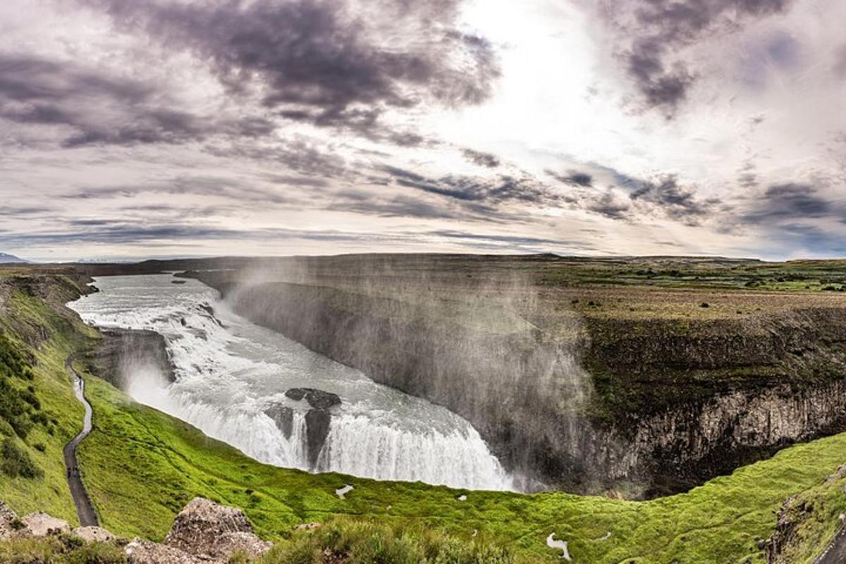 a waterfall on the side of a mountain with a cloudy sky