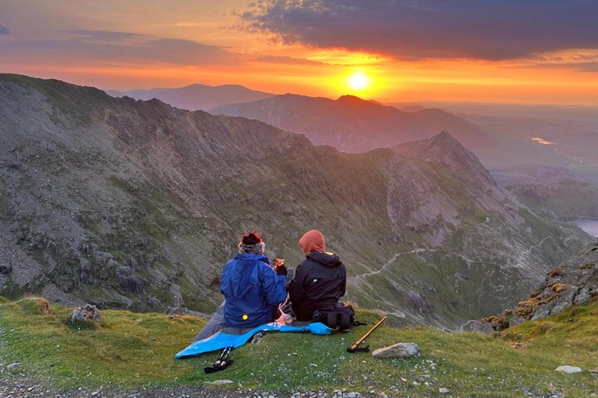 two people sitting on top of a mountain watching the sunset