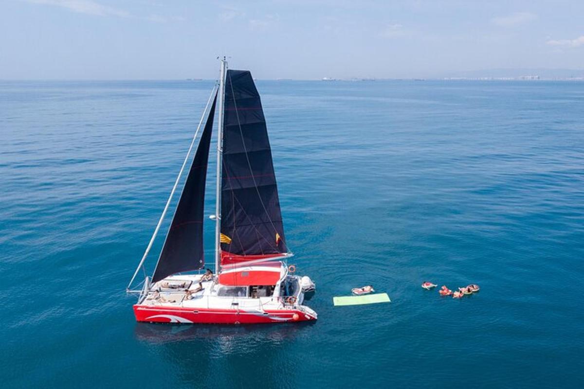 a red and white sailboat in the water with people swimming