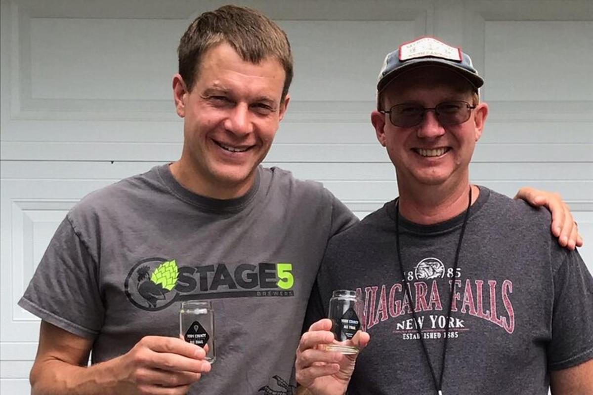 two men standing next to each other holding a bottle of beer