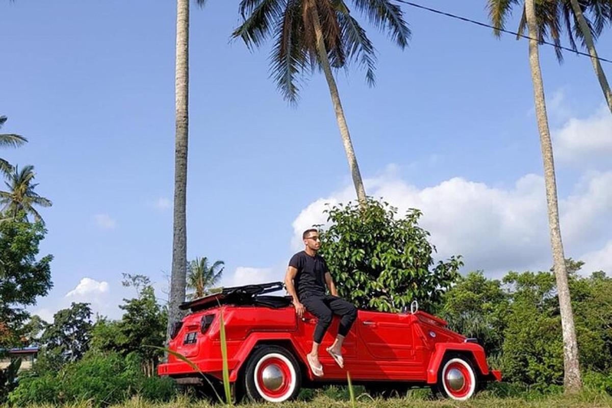 um homem sentado no capô de um carro vermelho com palmeiras