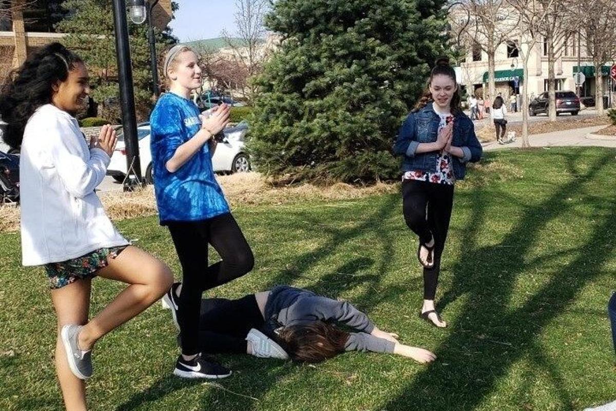 Un grupo de chicas de pie alrededor de una persona tumbada en el césped.