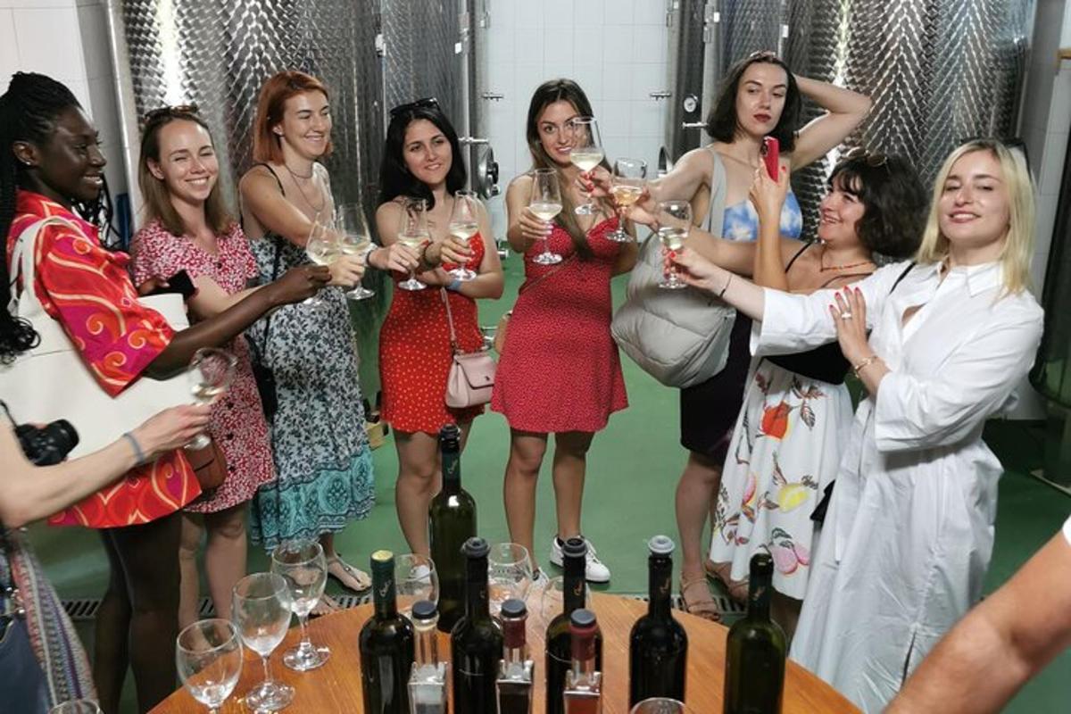 een groep vrouwen die rond een tafel staan en wijnglazen vasthouden