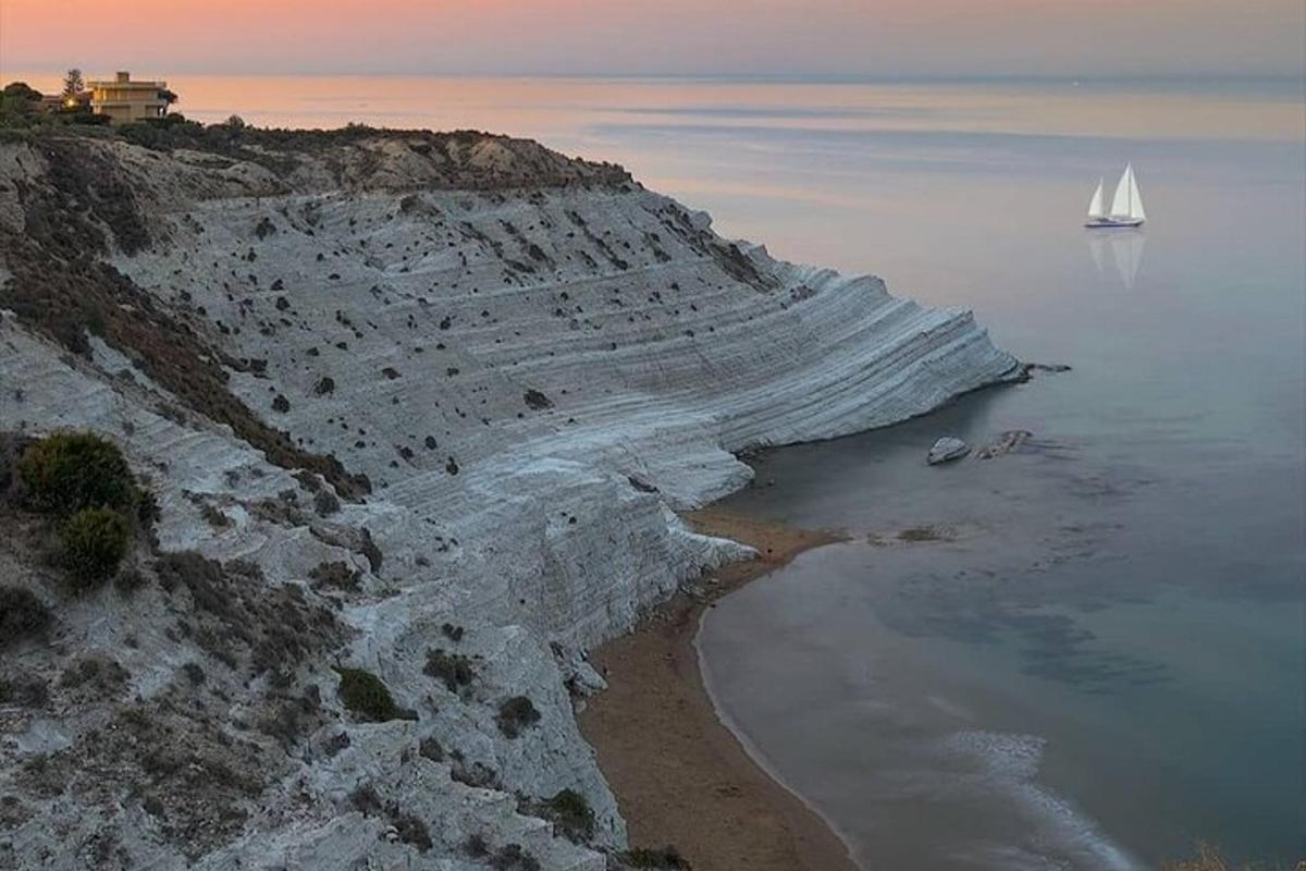 un veler a l'oceà al costat d'una costa rocosa