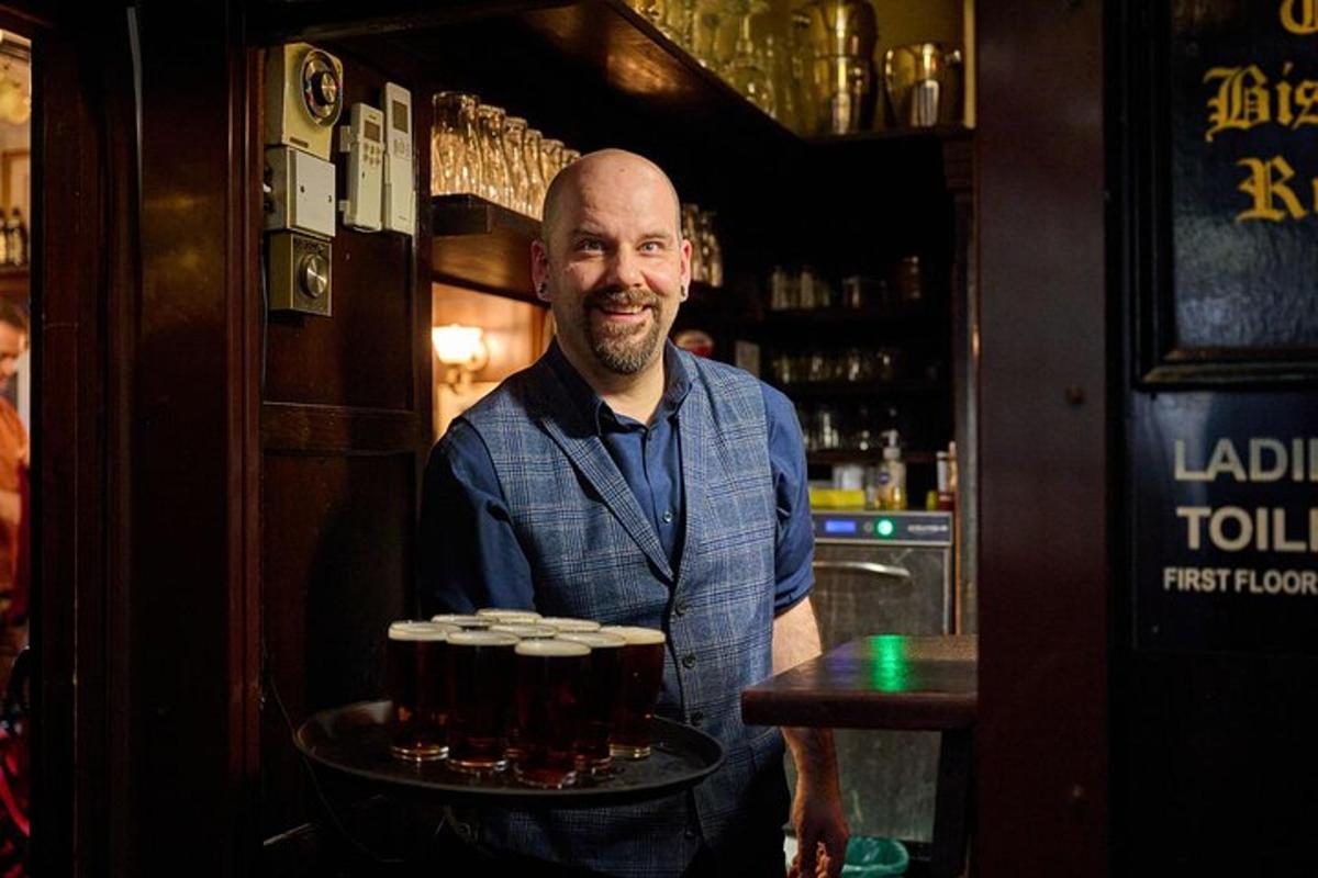en mann som står i en bar med et brett med øl