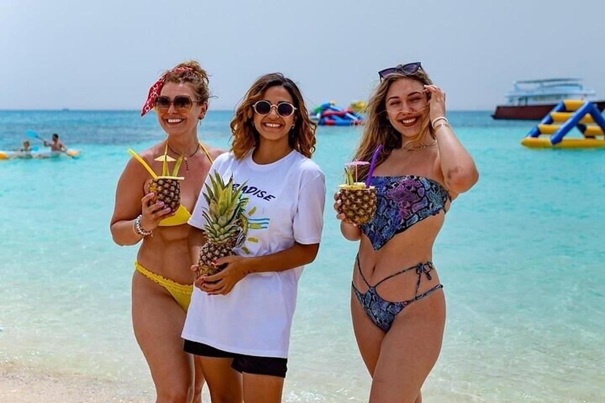 three women standing on the beach holding pineapple drinks