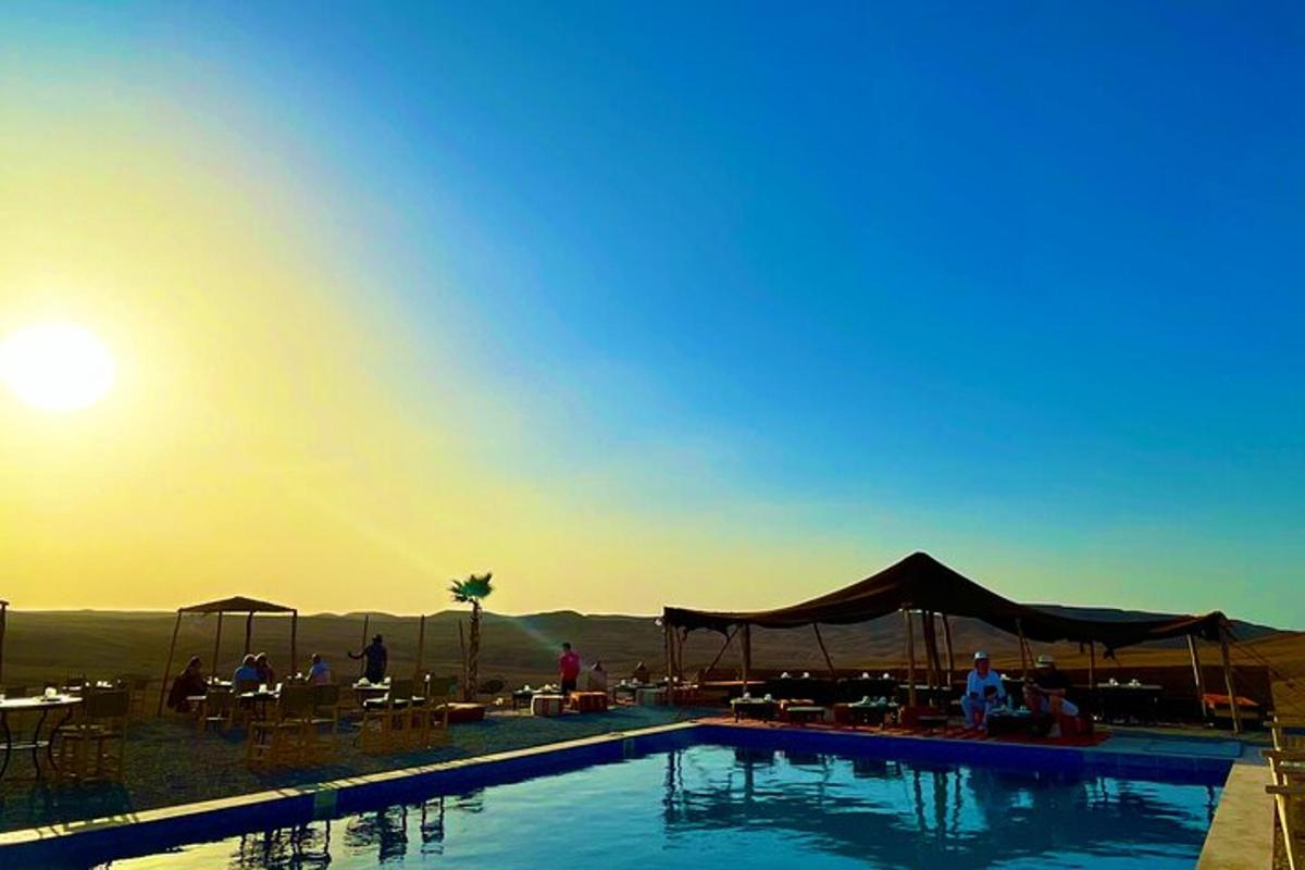 a swimming pool with people sitting around it with the sunset