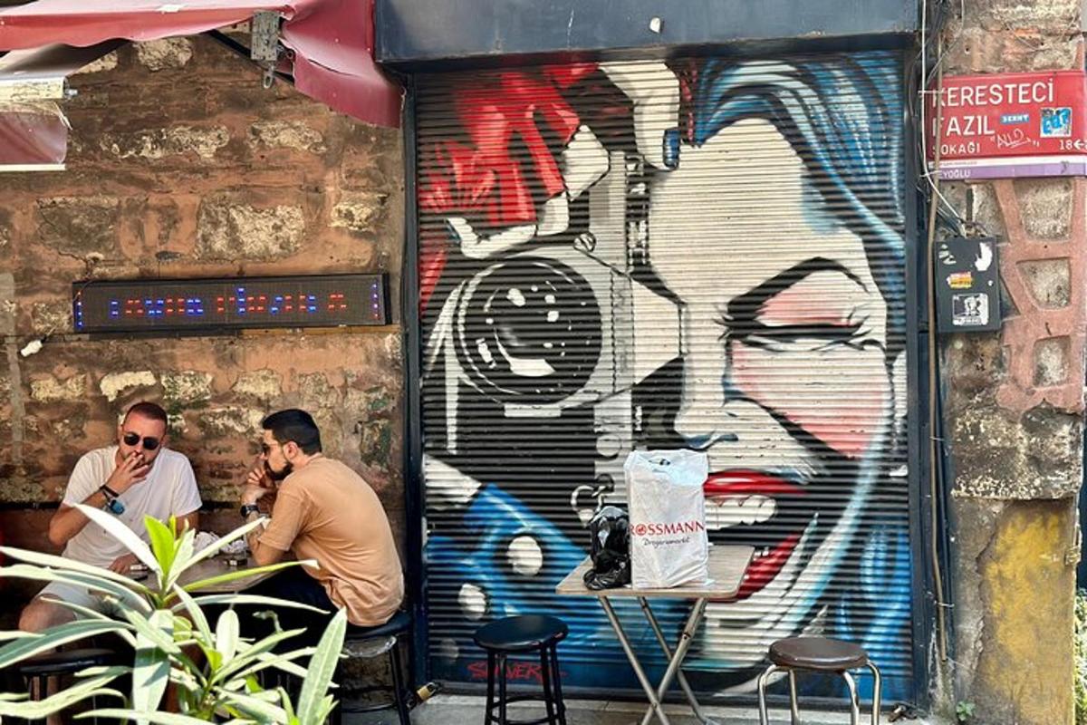 Két férfi ül egy asztalnál egy graffitivel borított fal előtt
