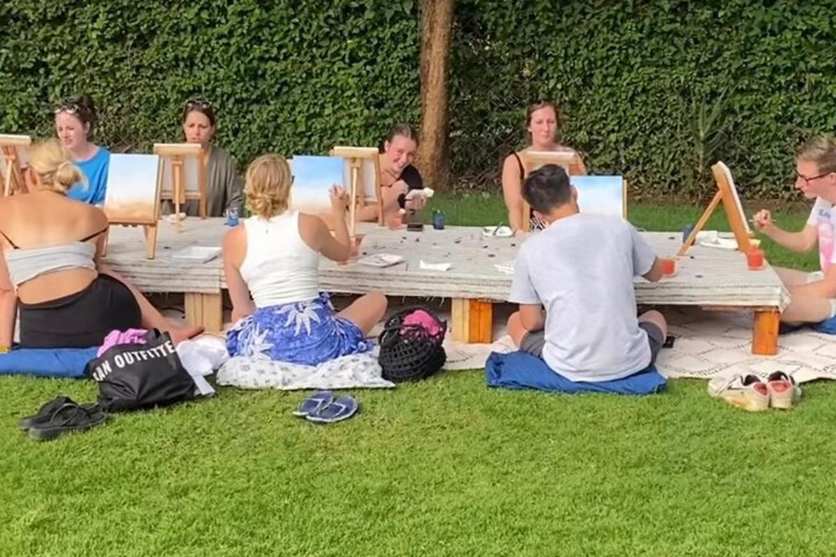 skupina lidí sedících kolem piknikového stolu na trávě