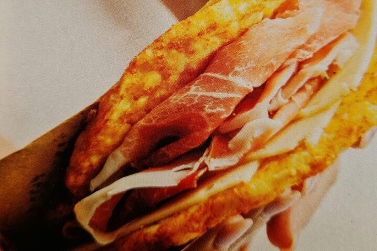a hand holding a sandwich with meat and cheese