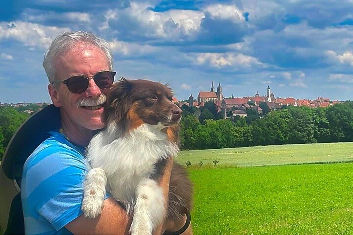 un uomo che tiene in braccio un cane marrone e bianco in un campo