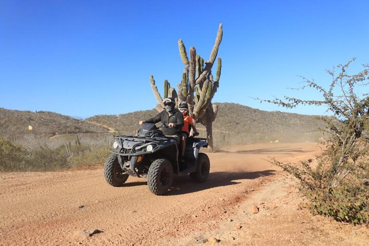 duas pessoas andando em um quadriciclo em uma estrada de terra