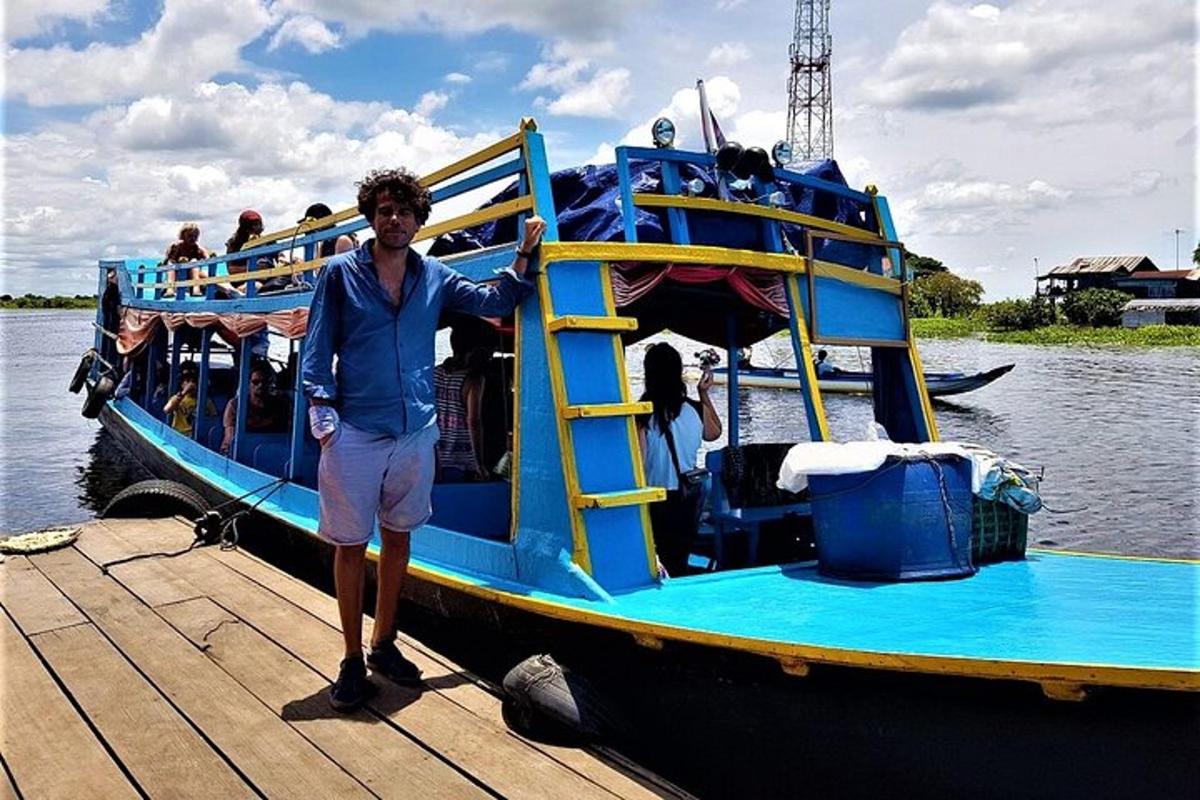 ชายคนหนึ่งยืนอยู่บนท่าเรือข้างเรือสีฟ้า