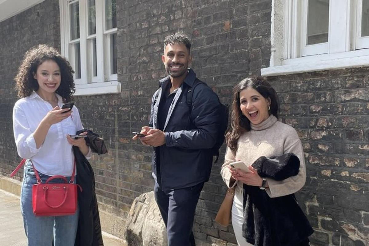 three people standing next to a brick building looking at their cell phones