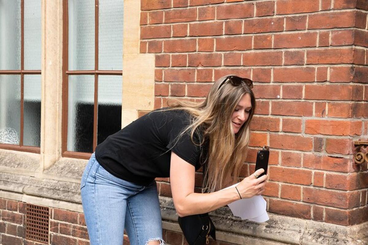 een vrouw die tegen een bakstenen muur leunt en naar haar mobiele telefoon kijkt