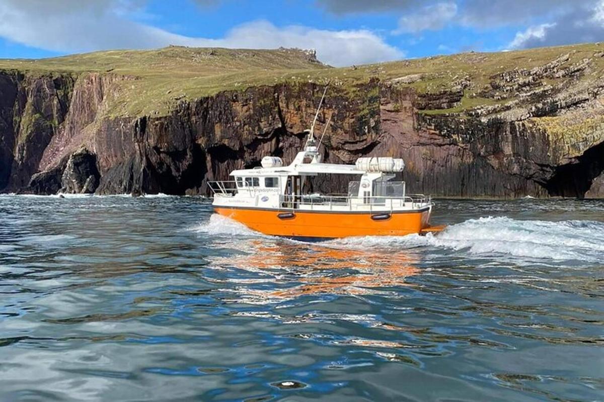 an orange and white boat in the water near a cliff