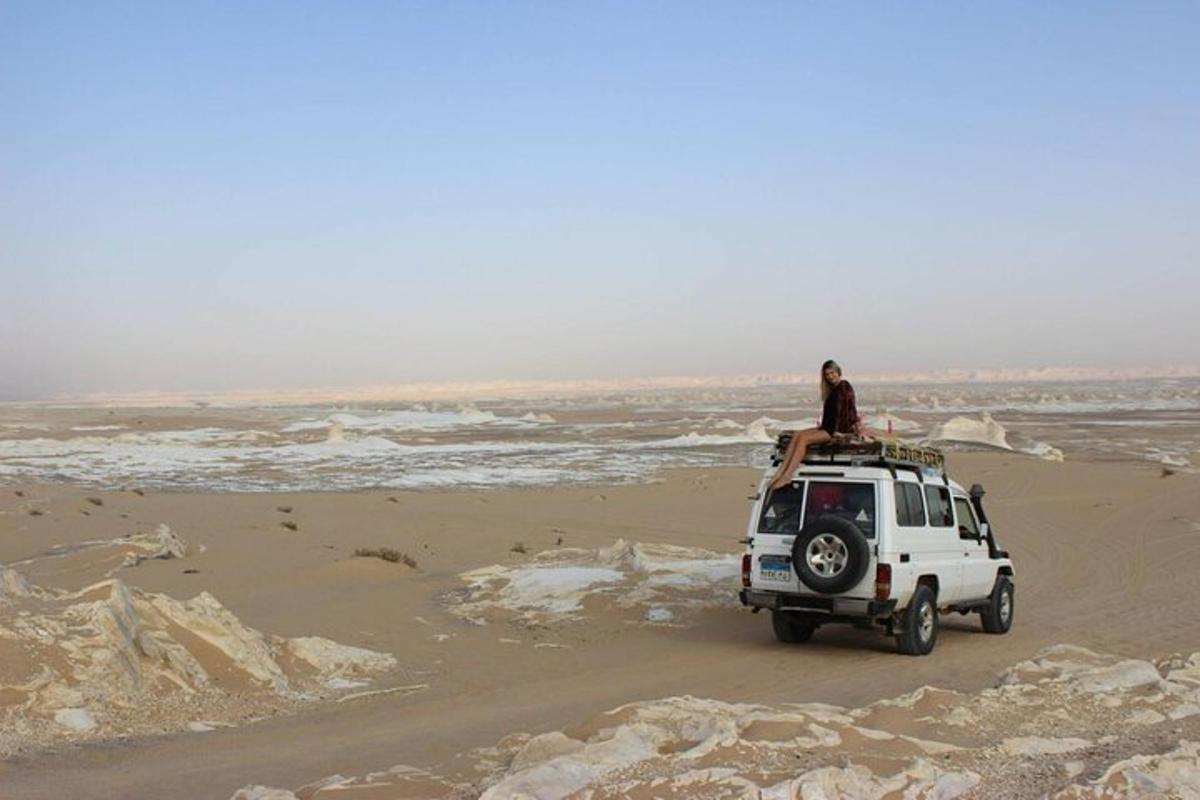 a person sitting on top of a white jeep on a beach