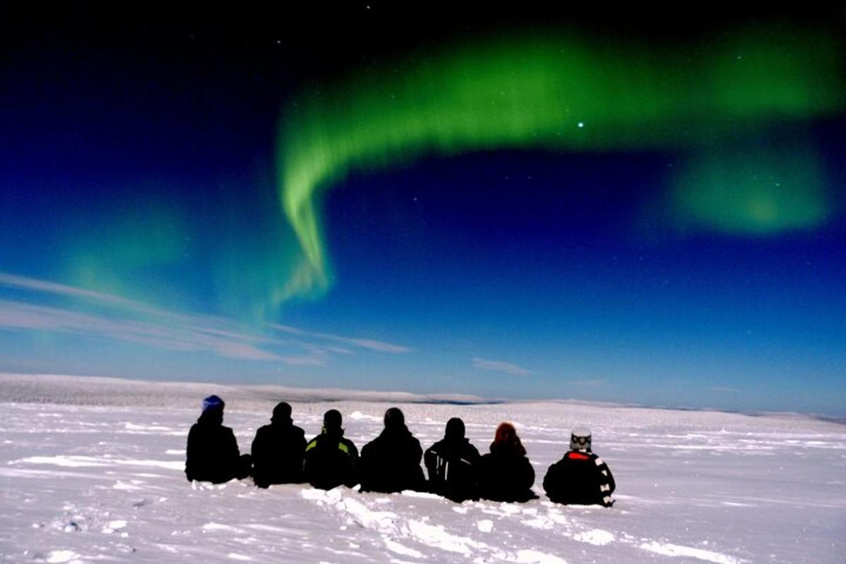 a group of people sitting in the snow watching the northern lights