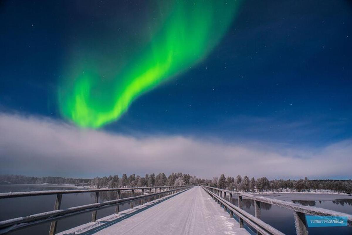 an icy road with a bridge with the green northern lights