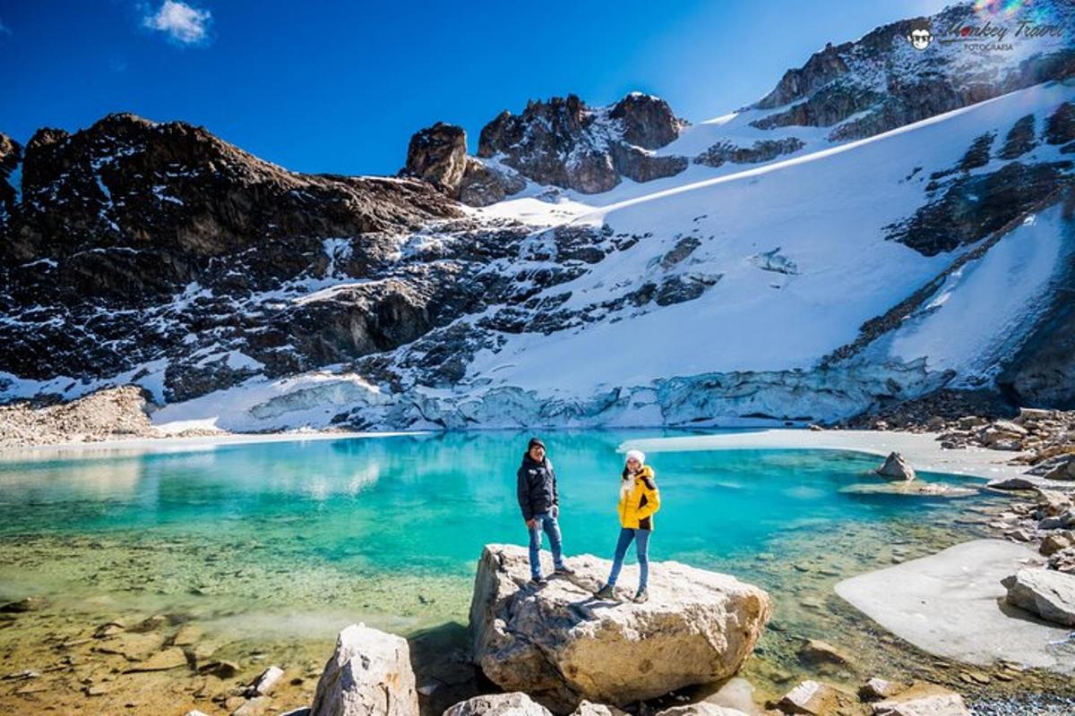 two people standing on rocks near a mountain lake