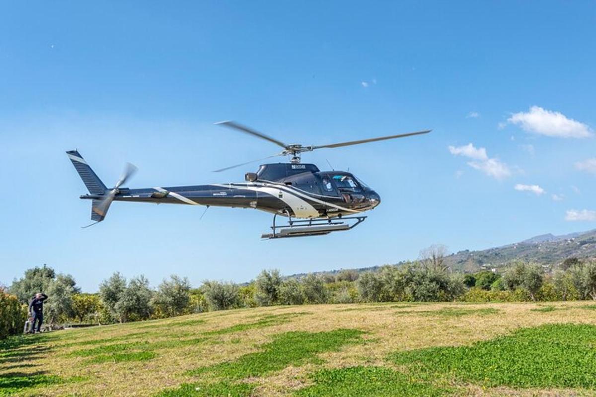un helicòpter sobrevolant un camp amb una persona dreta en un turó
