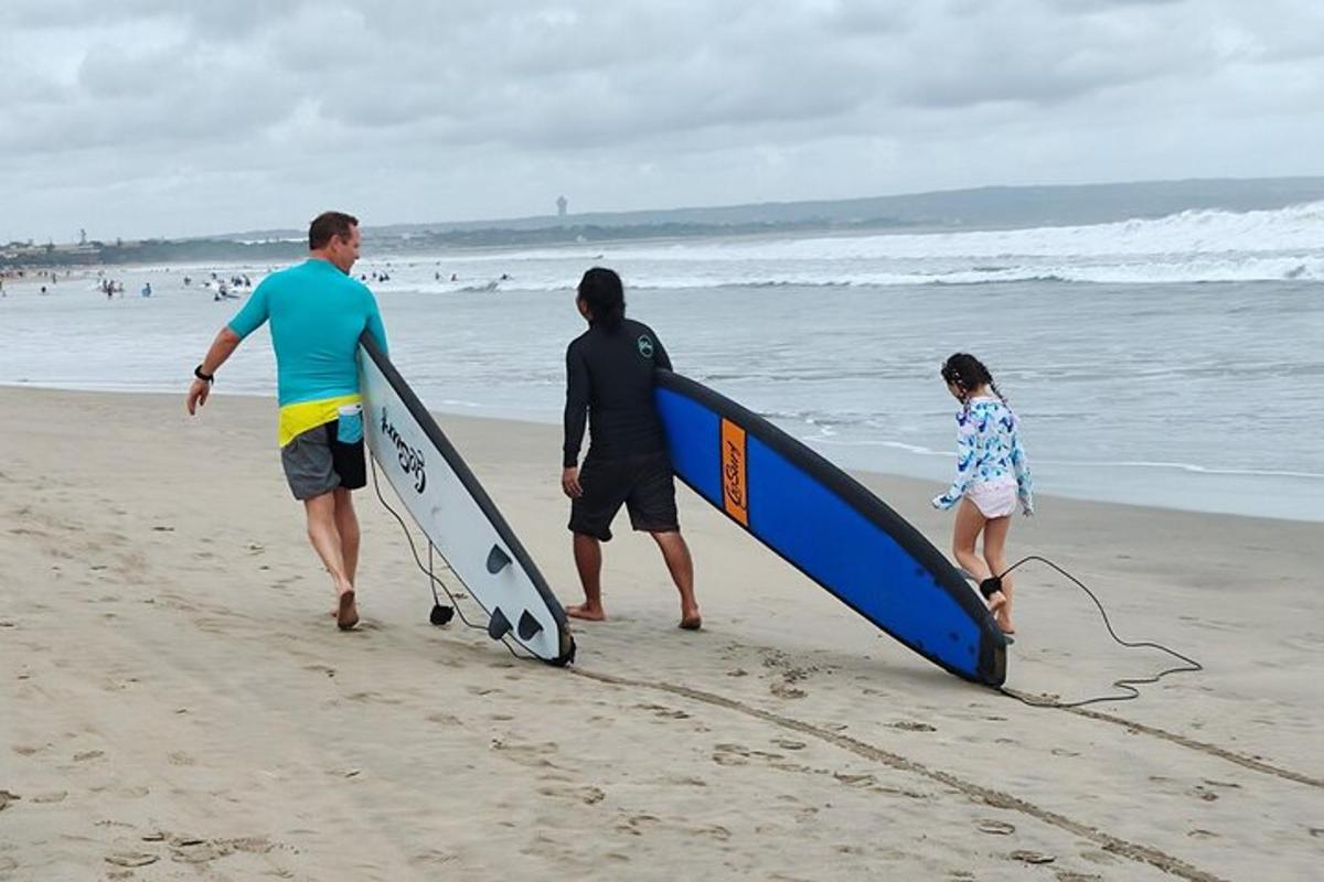 Dos hombres y una niña caminando por la playa con tablas de surf