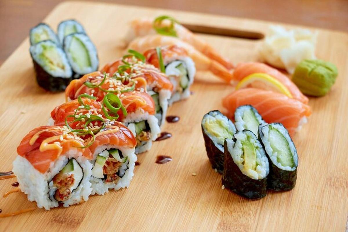 papan pemotong kayu dengan sushi dan sayur-sayuran di atasnya