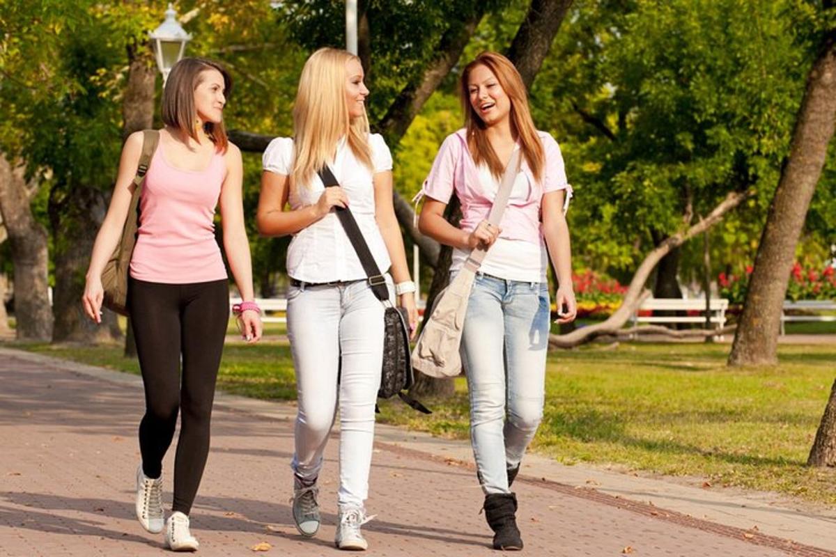 three girls walking down a sidewalk in a park