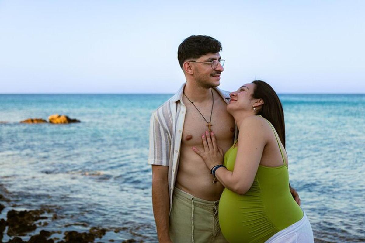 um homem e uma mulher grávida em pé na praia