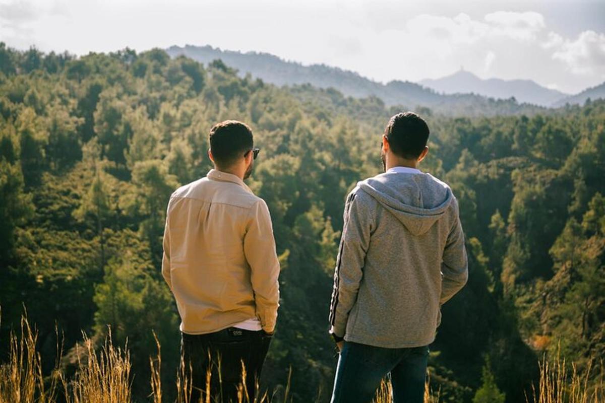 dois homens em pé no topo de uma colina com vista para uma floresta