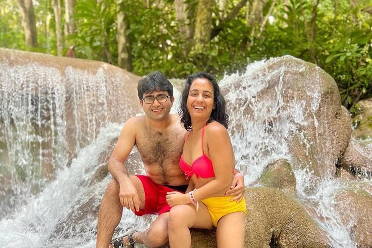 a man and woman sitting on a rock in front of a waterfall