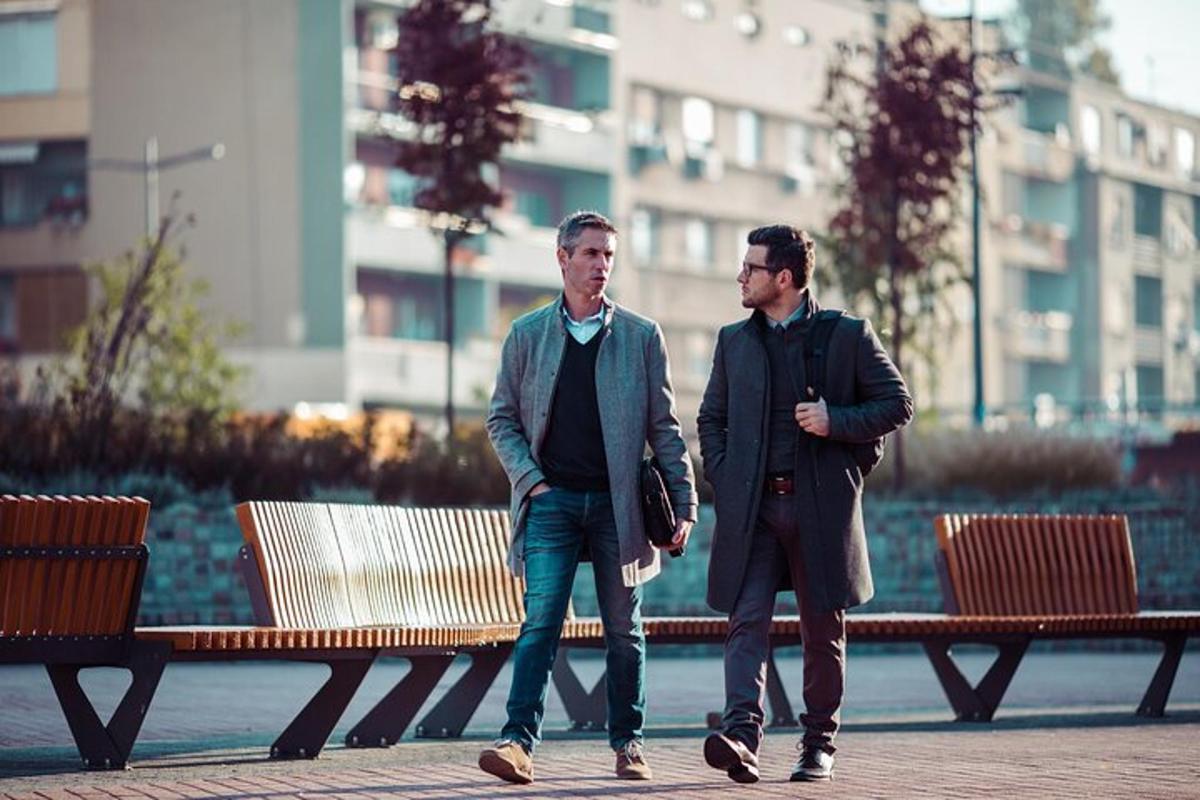 Dos hombres caminando por una acera junto a un banco
