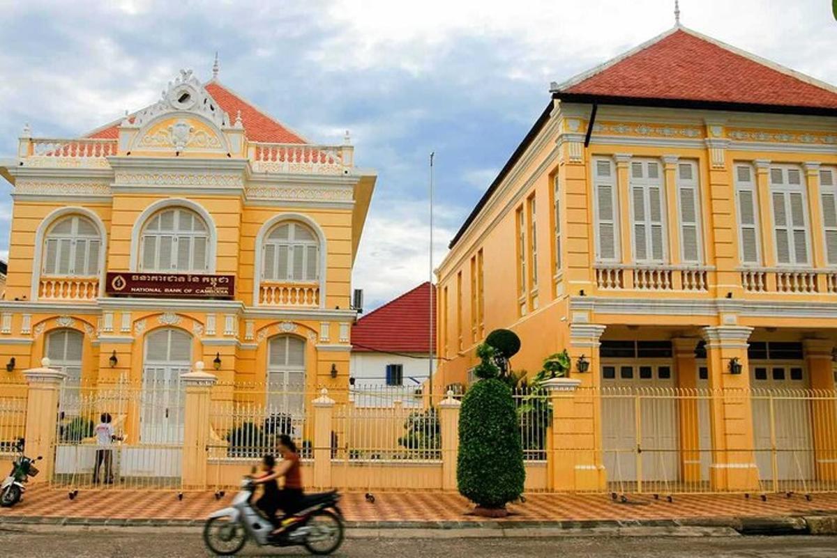 một người phụ nữ đang đi xe máy trước một tòa nhà màu vàng