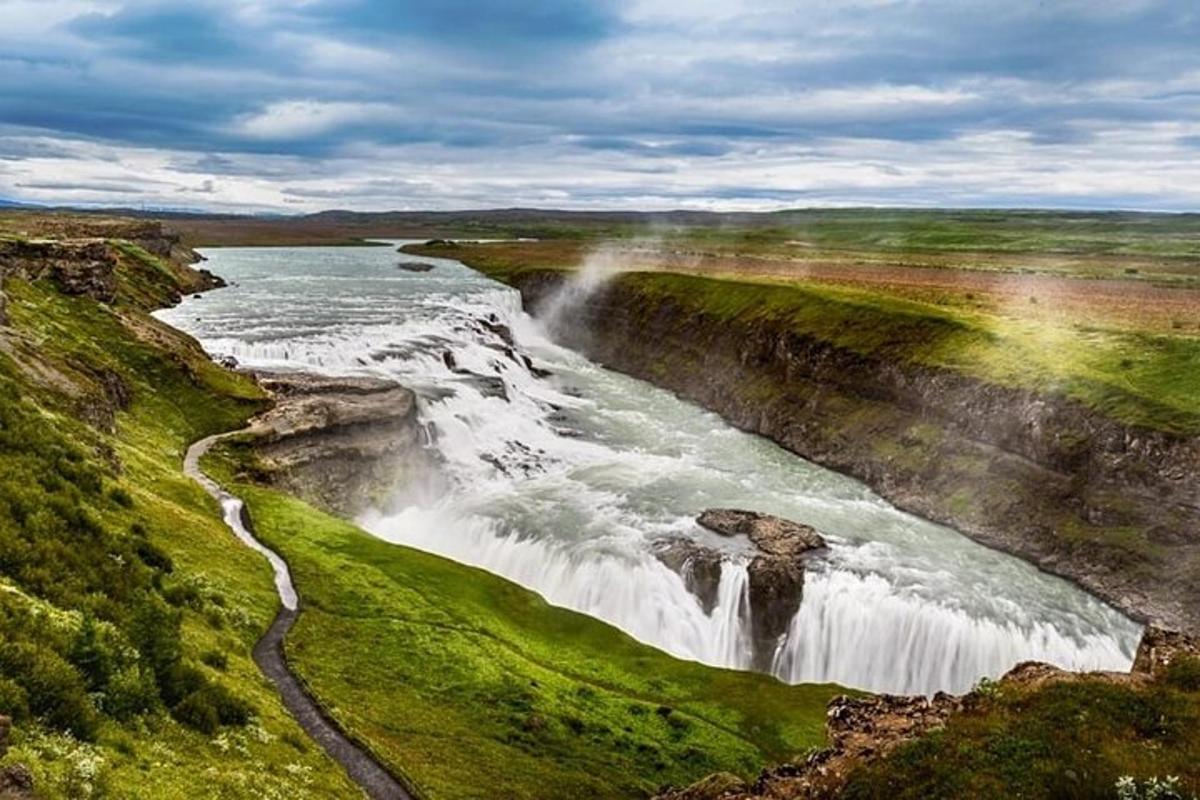 uma cachoeira com um arco-íris na margem de um rio