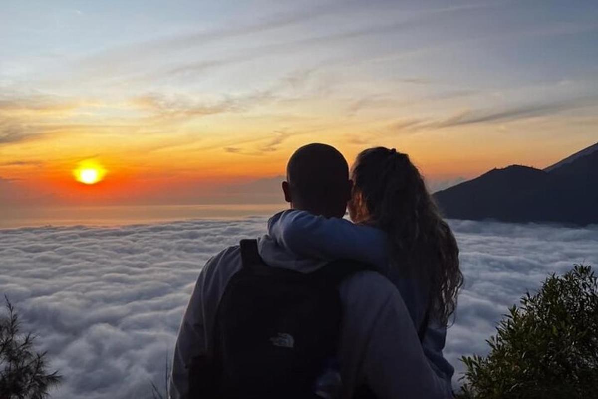muž a žena sedící na vrcholu hory a pozorující západ slunce