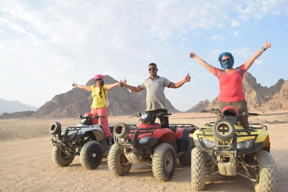 trei persoane pe ATV-uri în deșert cu brațele întinse