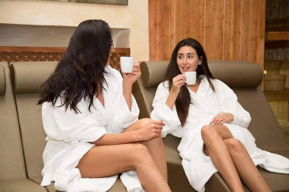 Dos mujeres sentadas en un sofá con toallas tomando café