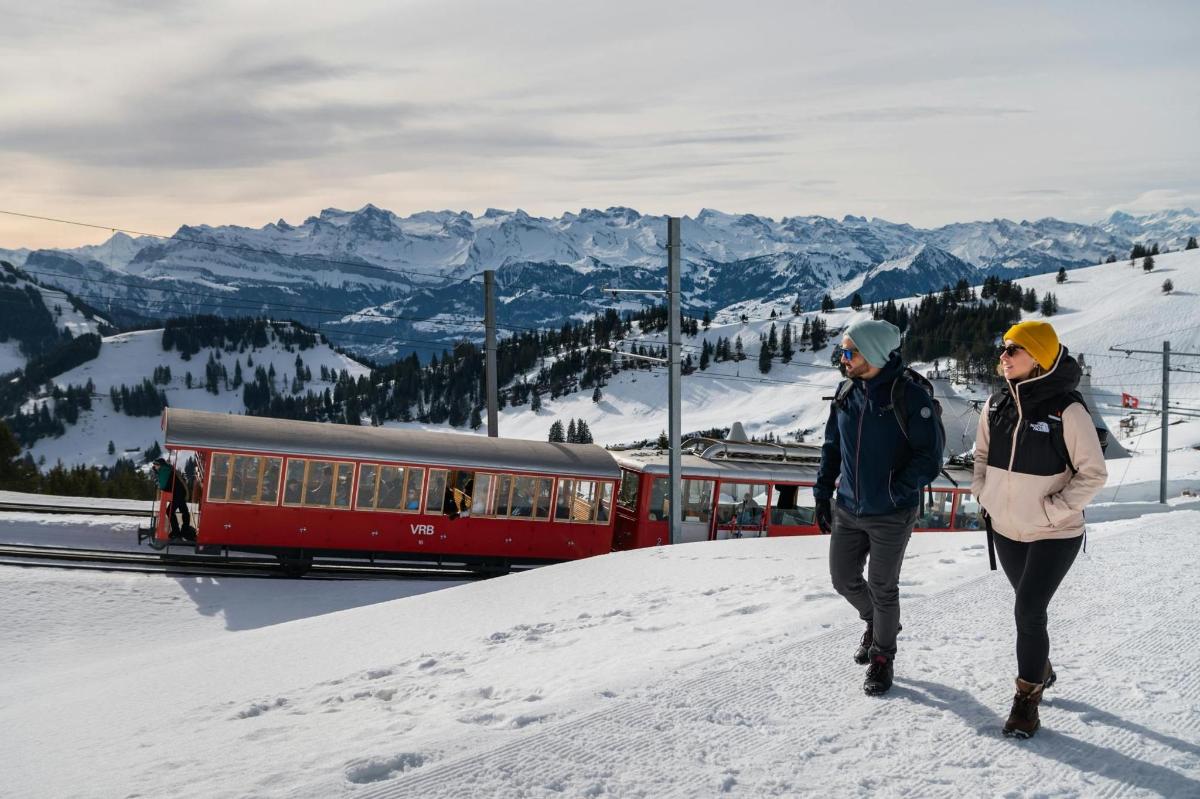 two people walking on the snow next to a train